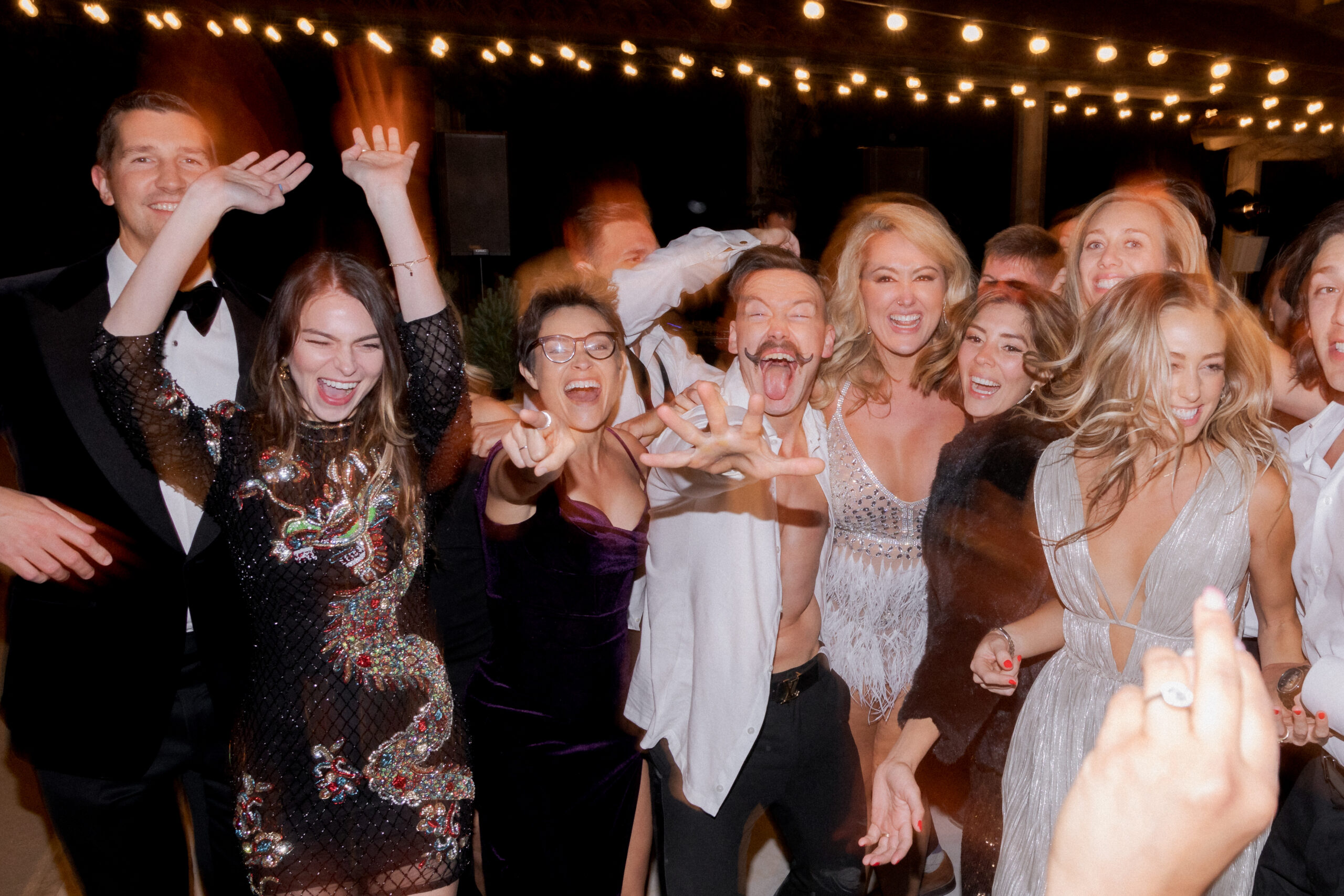 fun wedding reception dance floor photo of bride and groom and their friends laughing dancing and pointing at photographer